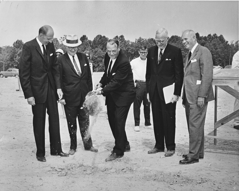 Men standing around a construction site. One is shoveling dirt.