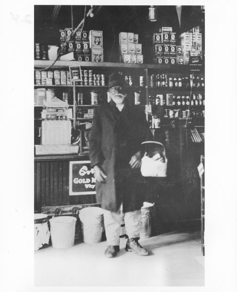 Portrait of James Lee standing inside a grocery store holding a basket, circa 1910.