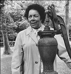 Marguerite Mott stands with outdoor water pump in 1983