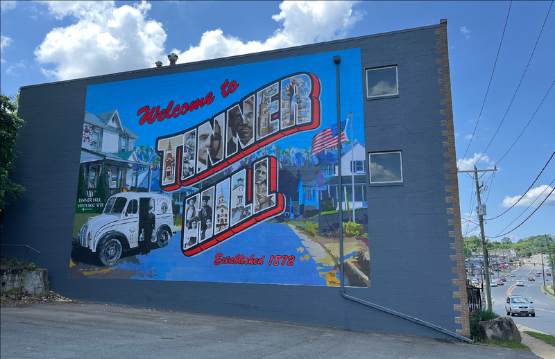 Side exterior of a building in Falls Church, Virginia with a brightly colored mural with the words "Tinner Hill" painted by Bryan King, circa 2024.
