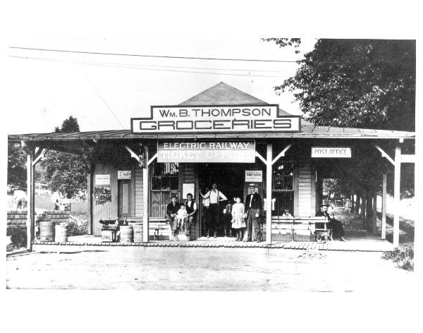 Exterior of the East Falls Church trolley station. Multiple people stand in the doorway looking in the direction of the camera. Circa 1910.