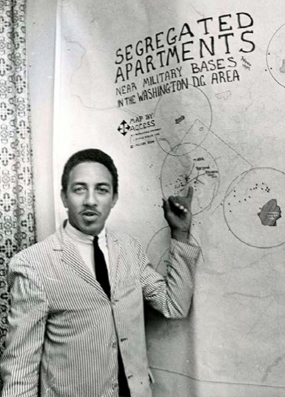 Photograph of ACCESS Chairman Charles Jones in front of a poster in 1967.