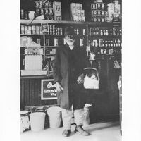 Portrait of James Lee standing inside a grocery store holding a basket, circa 1910.