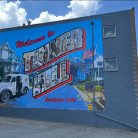 Side exterior of a building in Falls Church, Virginia with a brightly colored mural with the words "Tinner Hill" painted by Bryan King, circa 2024.